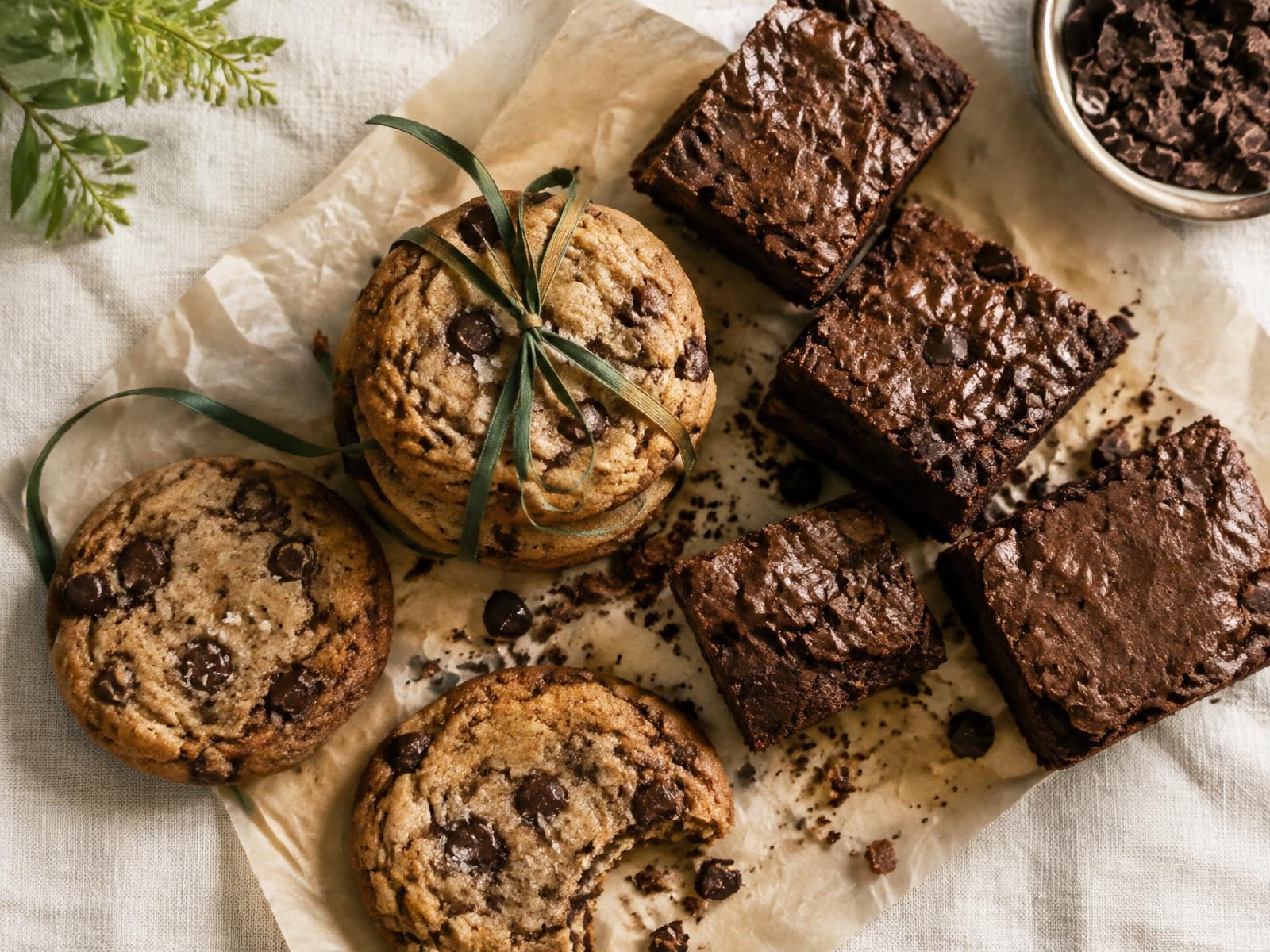 Chocolate chip cookies tied with a green ribbon beside a row of fudgy brownies